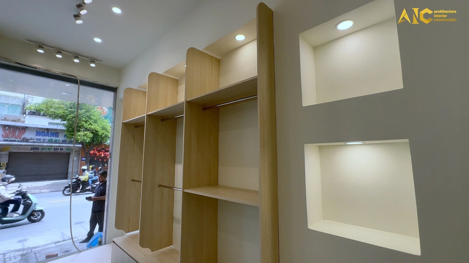 Tổng thể không gian trưng bày cửa hàng thời trang với hệ thống tủ gỗ be nhạt ấm cúng